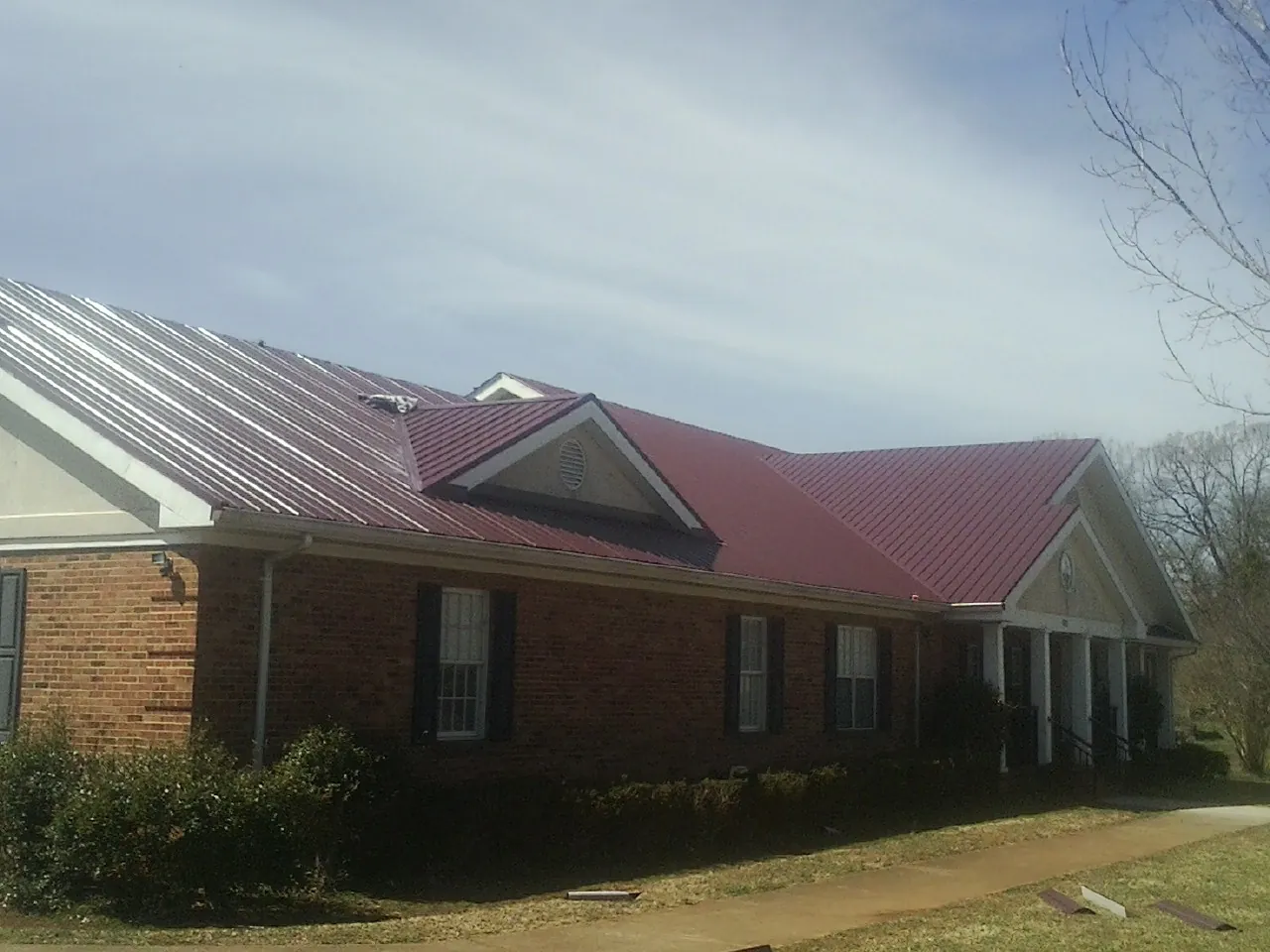 Red metal roof with gabled entries on a long brick building, from a Hail Damage Roof Repair job in Shacklefords