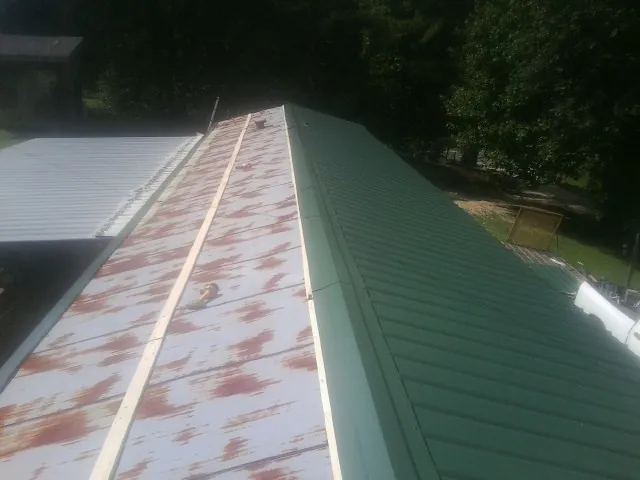 Old rusted panels beside newly installed green metal roofing — Wind Damage Roof Repair by Roofing Brothers in Shacklefords