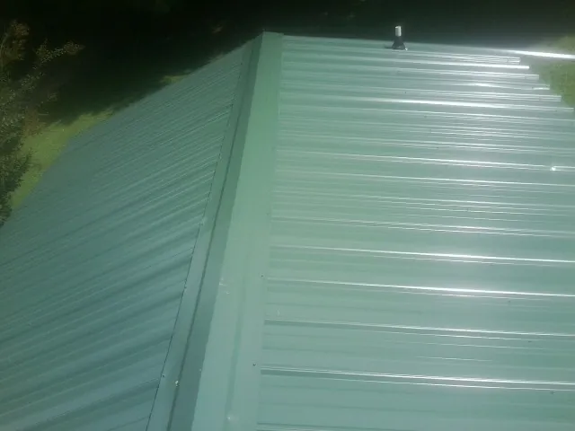 New green metal panels meeting at the ridge of a roof — Flat Roof Repair work by our crew in Shacklefords
