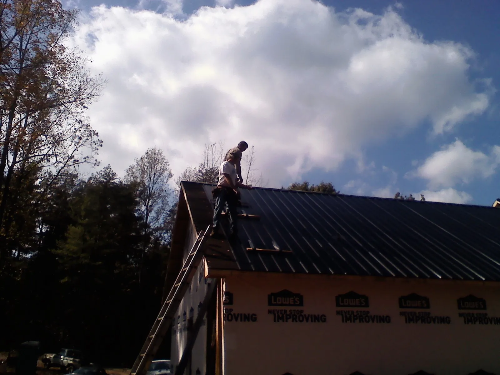 Roofer fastening dark metal panels high against a cloudy sky, from a Roof Inspection job in Shacklefords
