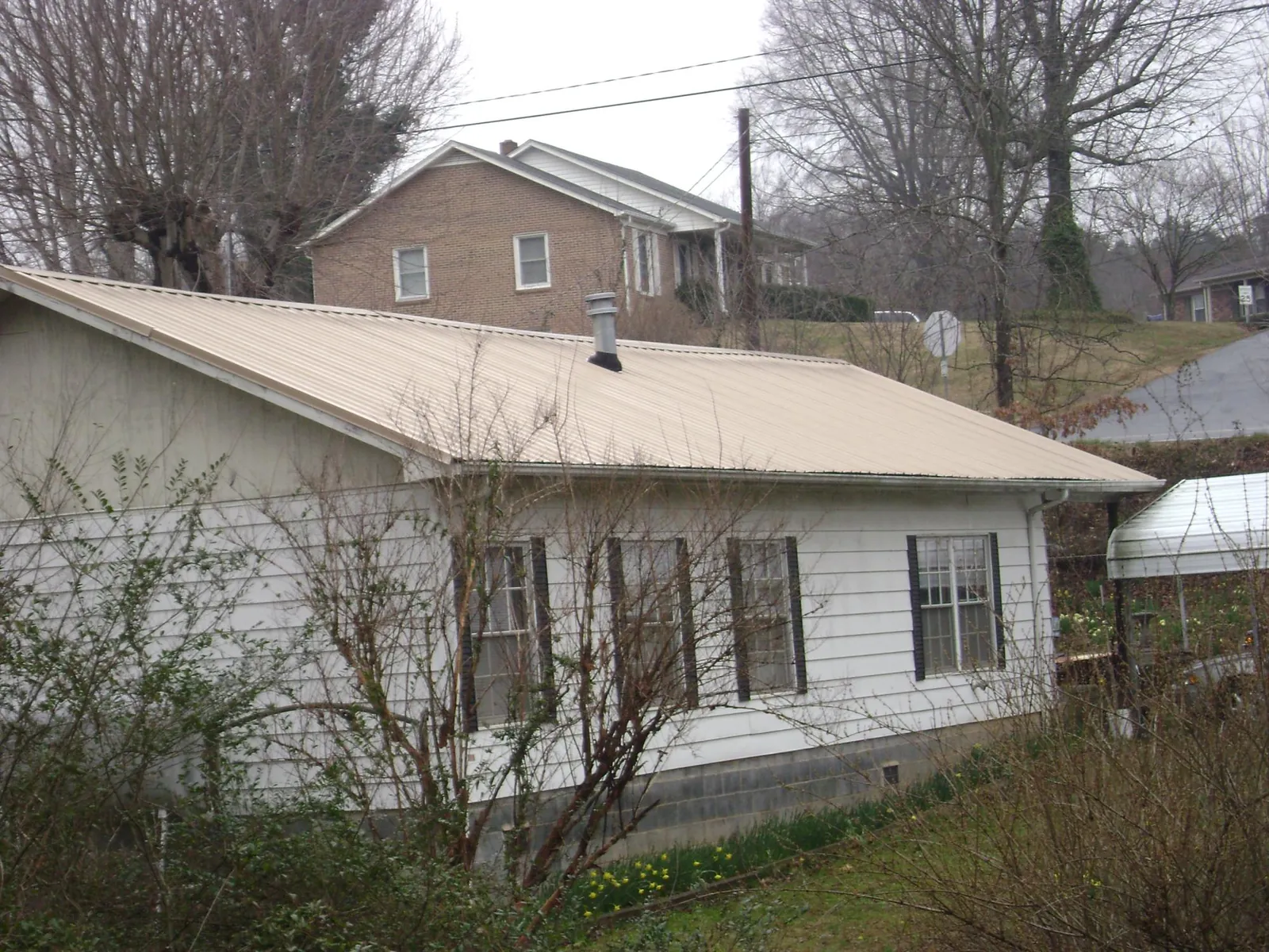 Tan metal roof on a white sided house set into a hillside — Commercial Roofing by Roofing Brothers in Shacklefords