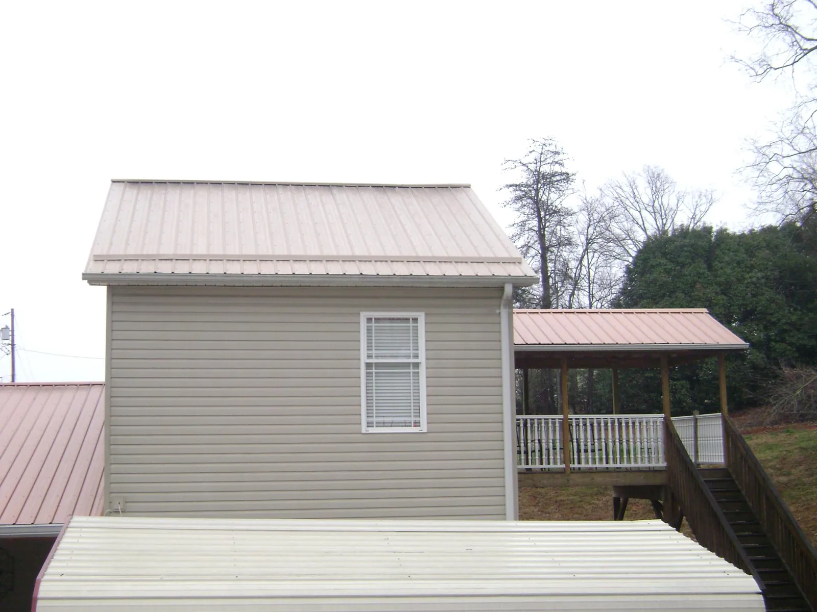 Tan metal roofs on a two story addition and attached porch, from a Roof Replacement job in Shacklefords
